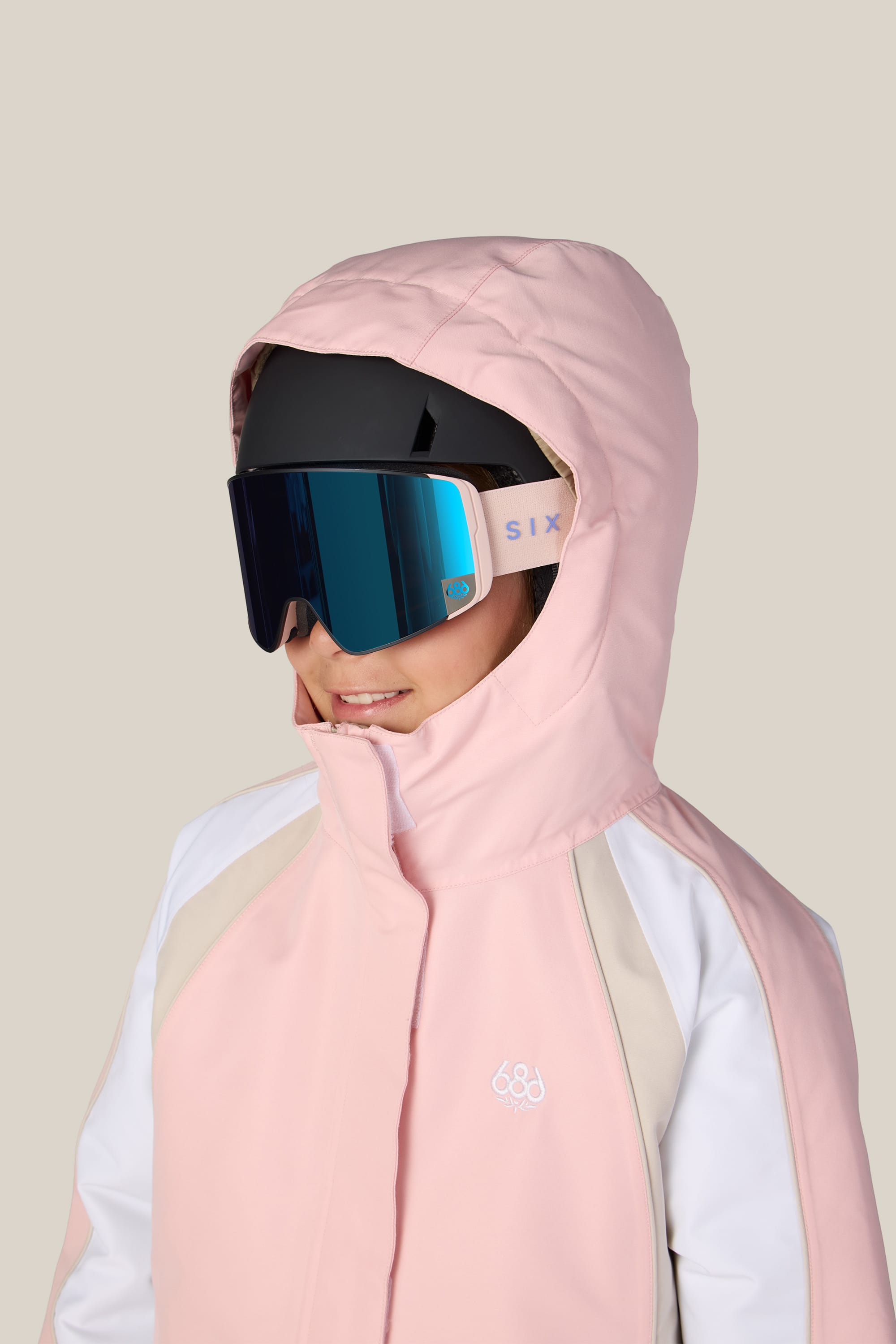 A child wearing the 686 Girls’ Hologram™ Insulated Jacket in light pink with a hood, paired with large reflective ski goggles, looks slightly to the side against a plain background.