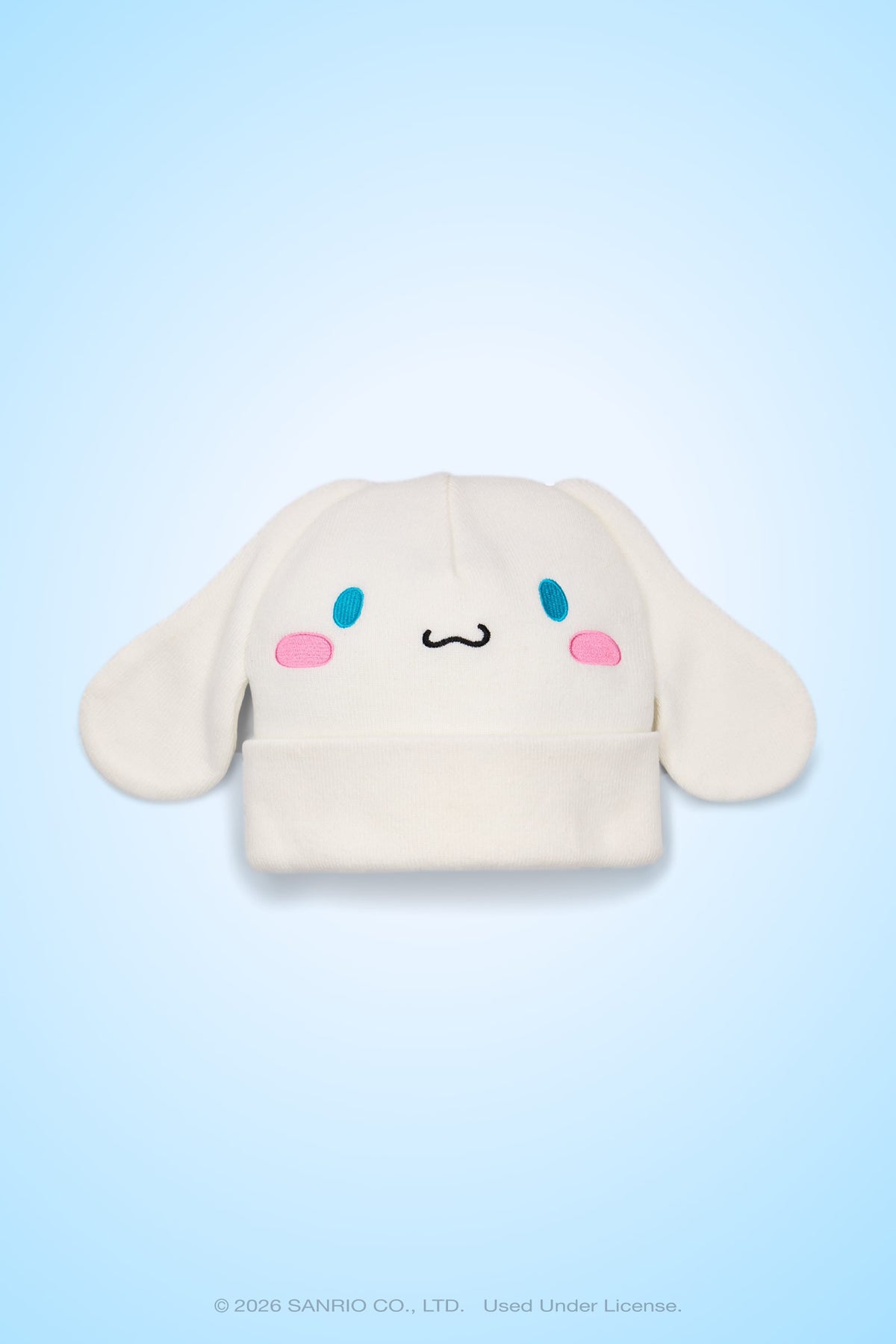 The 686 Women’s Cinnamoroll™ Beanie by 686 features a white acrylic knit design with floppy ears, blue oval eyes, pink cheeks, and a small smiling mouth that resembles the cute cartoon character Cinnamoroll, shown against a light blue background.