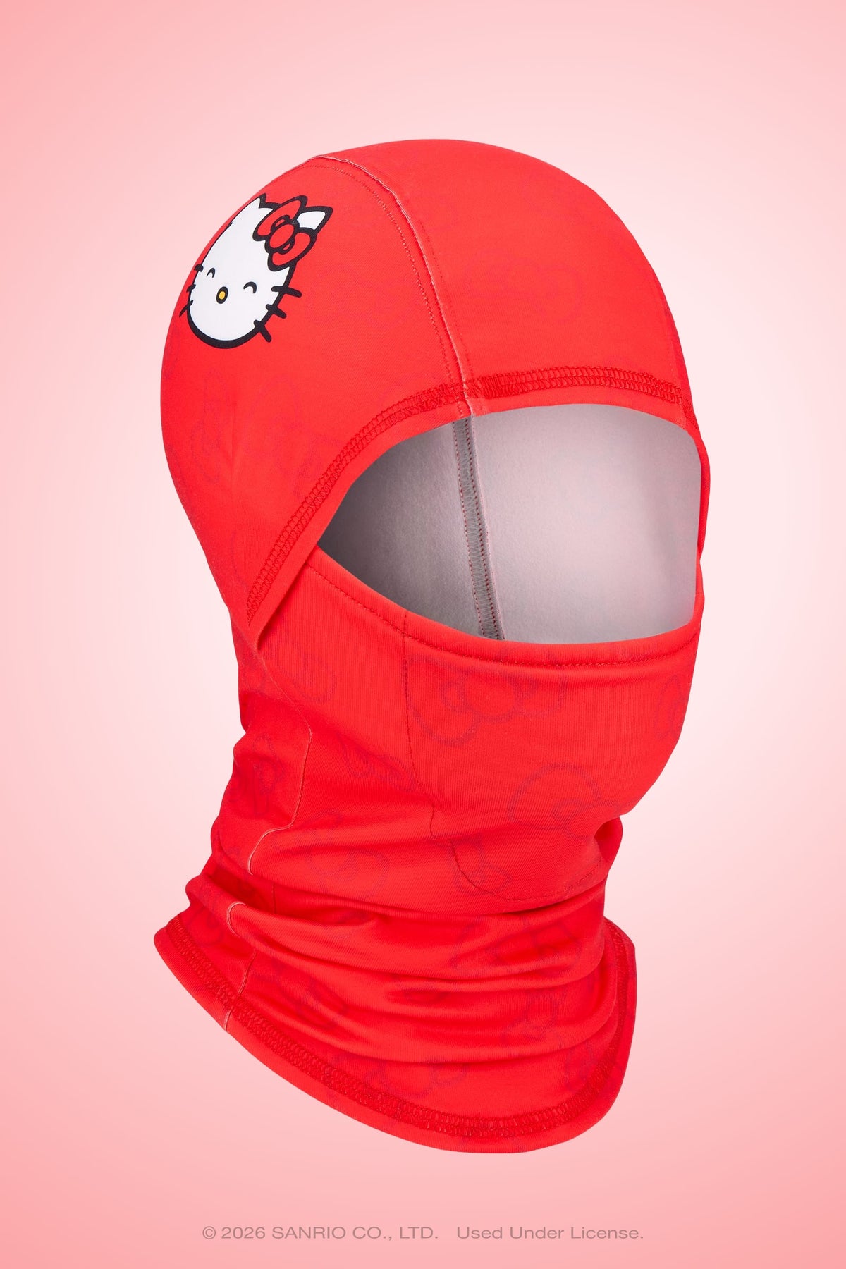 A vibrant red 686 Hurra Hinged Balaclava from 686, featuring the Hello Kitty face and bow on the forehead, is showcased on a faceless mannequin against a soft pink gradient background.