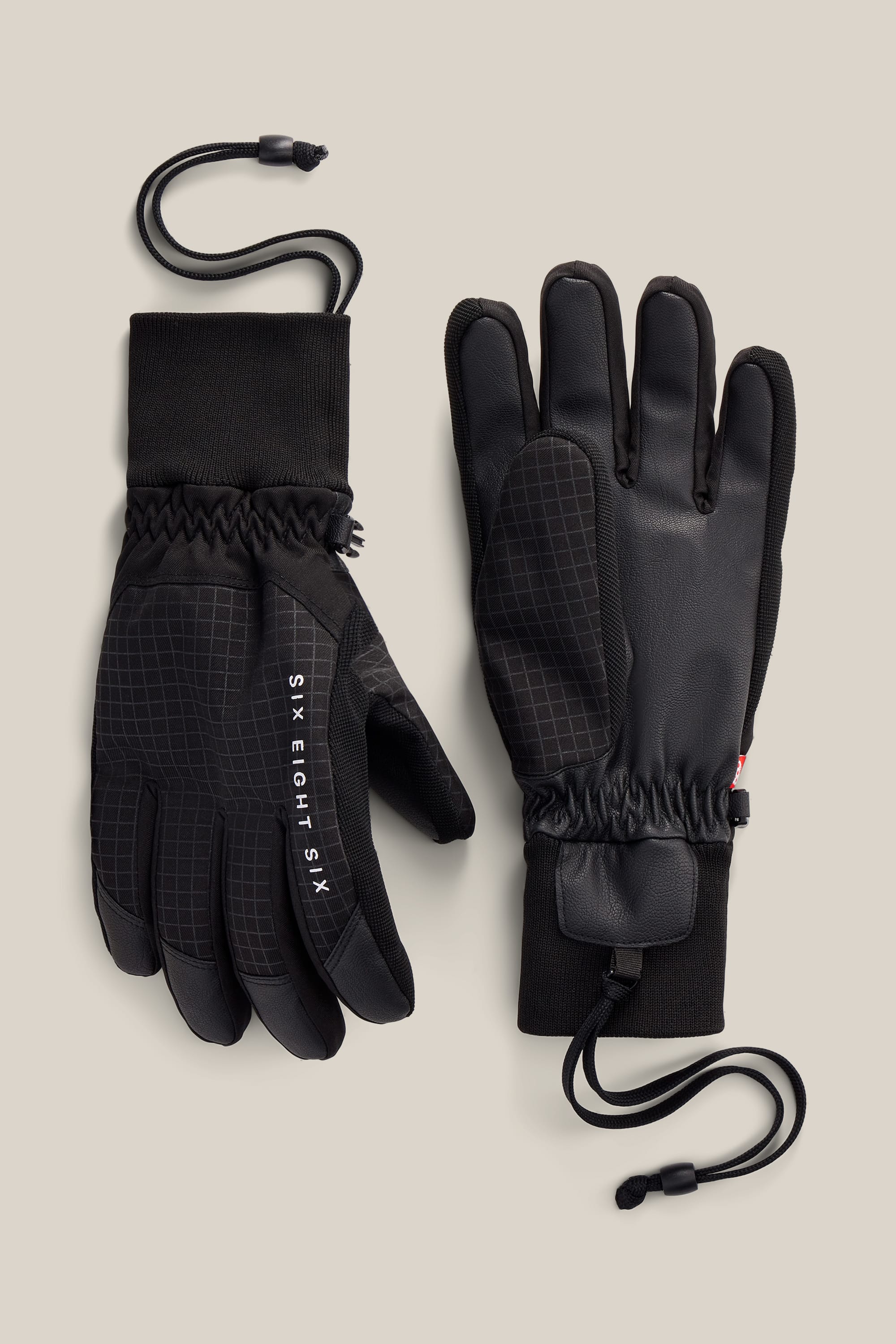 A pair of 686 Men’s Crush Insulated Gloves in black, featuring textured palms, elastic wrists, wrist leashes, and 686 branding on the back of one glove. Crafted with a durable PU construction and displayed against a neutral background.