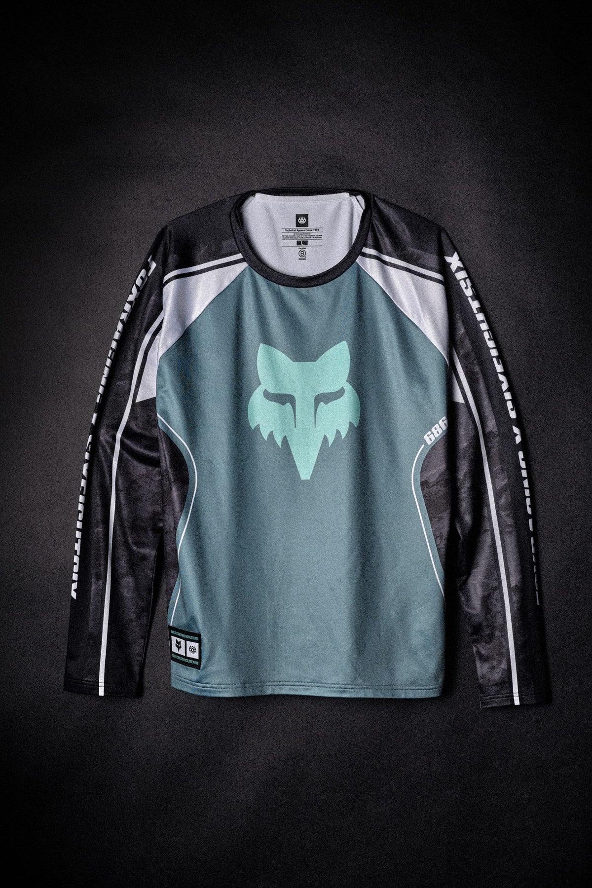 686 Men’s Fox Racing Base Layer LS featuring a teal Fox Racing logo on the chest and SIX EIGHT SIX branding on the sleeves.