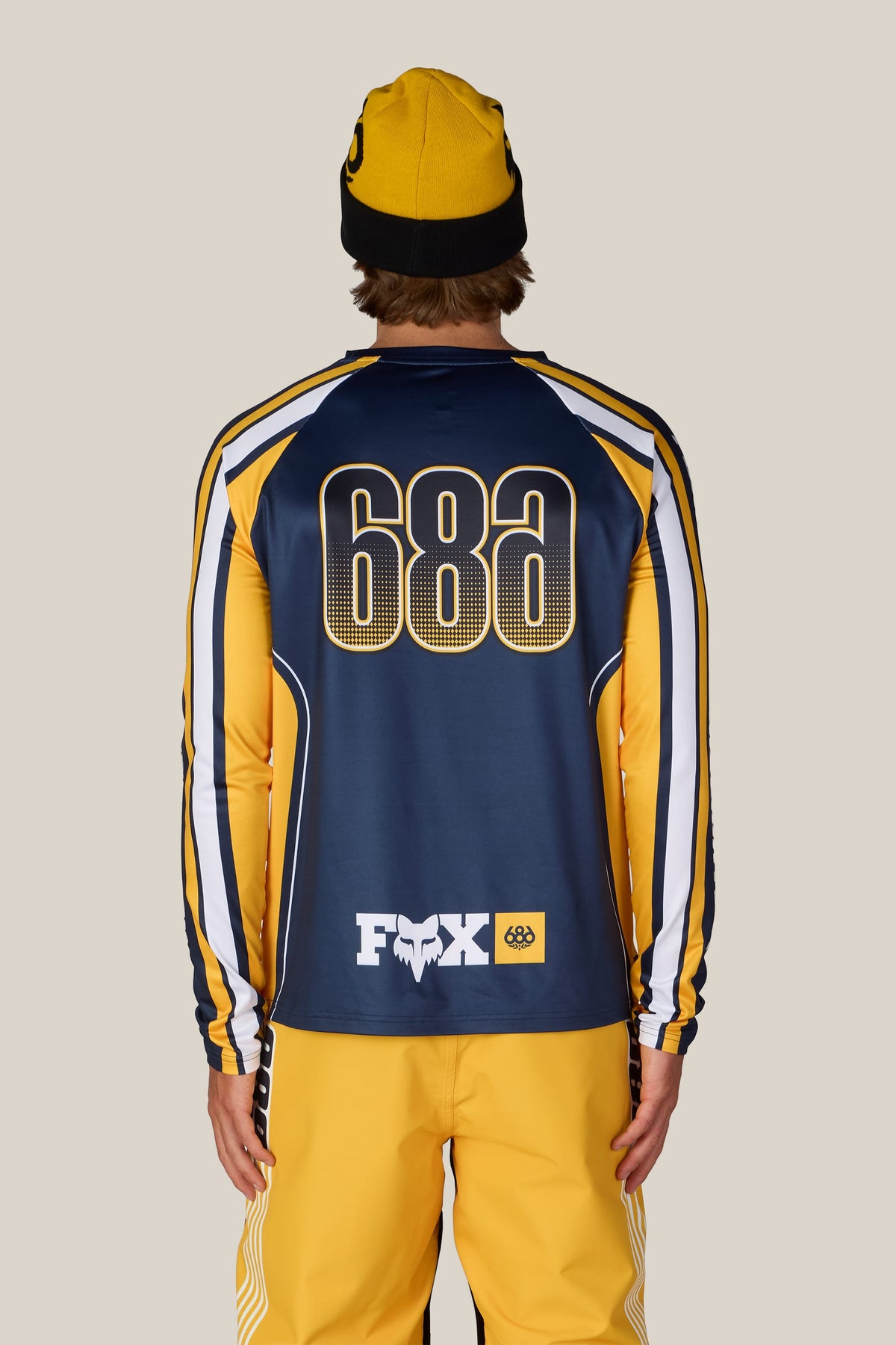 A person seen from the back wearing a 686 Men’s Fox Racing Base Layer LS and a yellow beanie.
