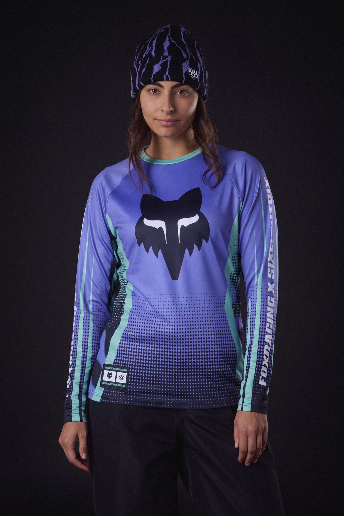A woman wearing a 686 Women’s Fox Racing Base Layer LS and a patterned beanie.