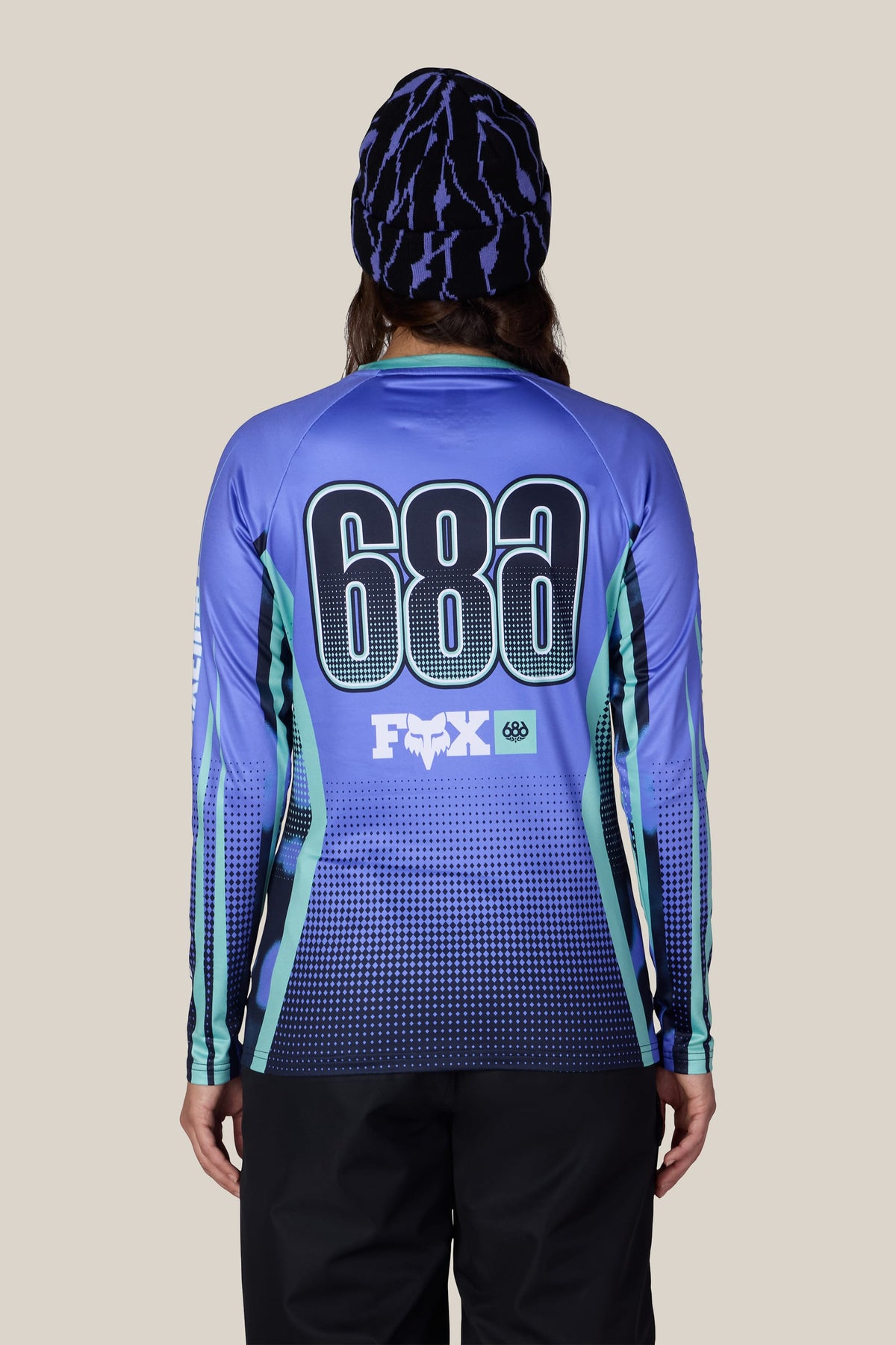 A person seen from behind wearing a 686 Women’s Fox Racing Base Layer LS and a patterned beanie.