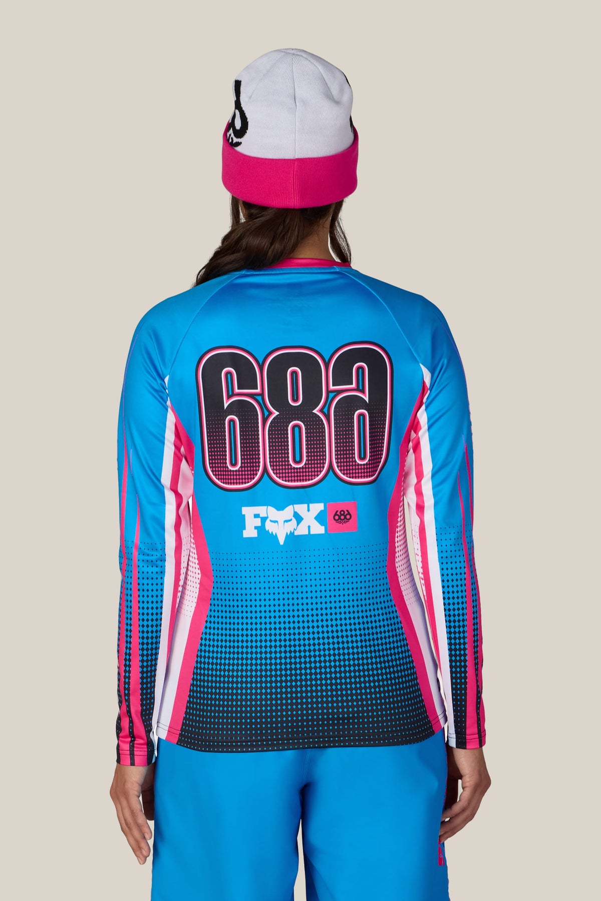 A person wearing a 686 Women’s Fox Racing Base Layer LS and a pink and white beanie.