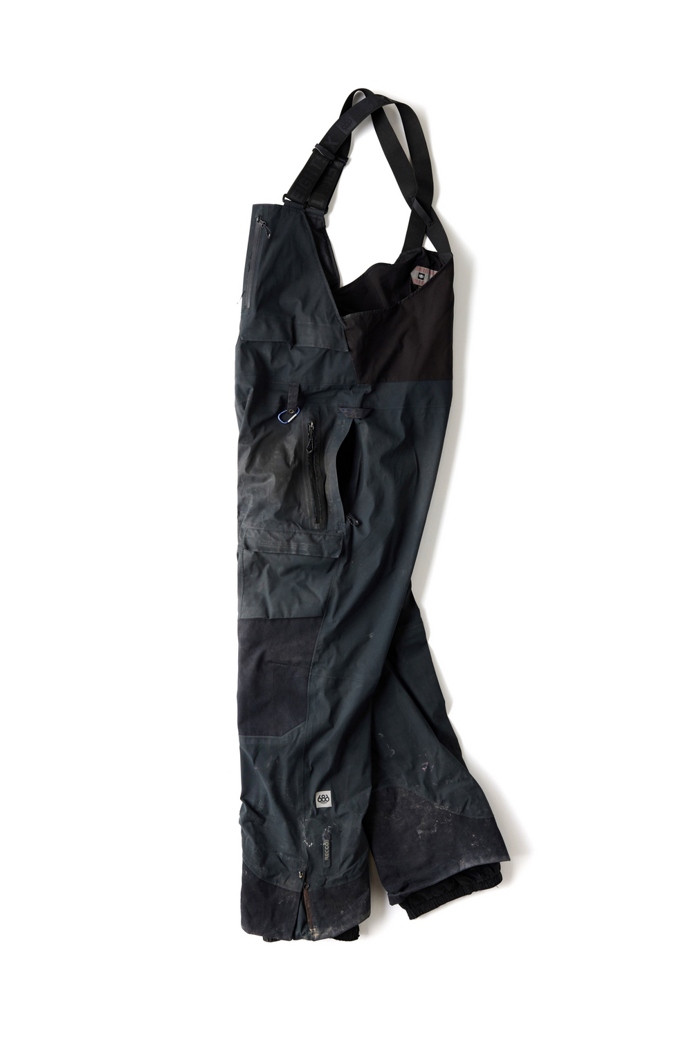 A pair of dark-colored work overalls with adjustable shoulder straps, multiple zippered pockets, and reinforced knee patches, laid flat against a white background.