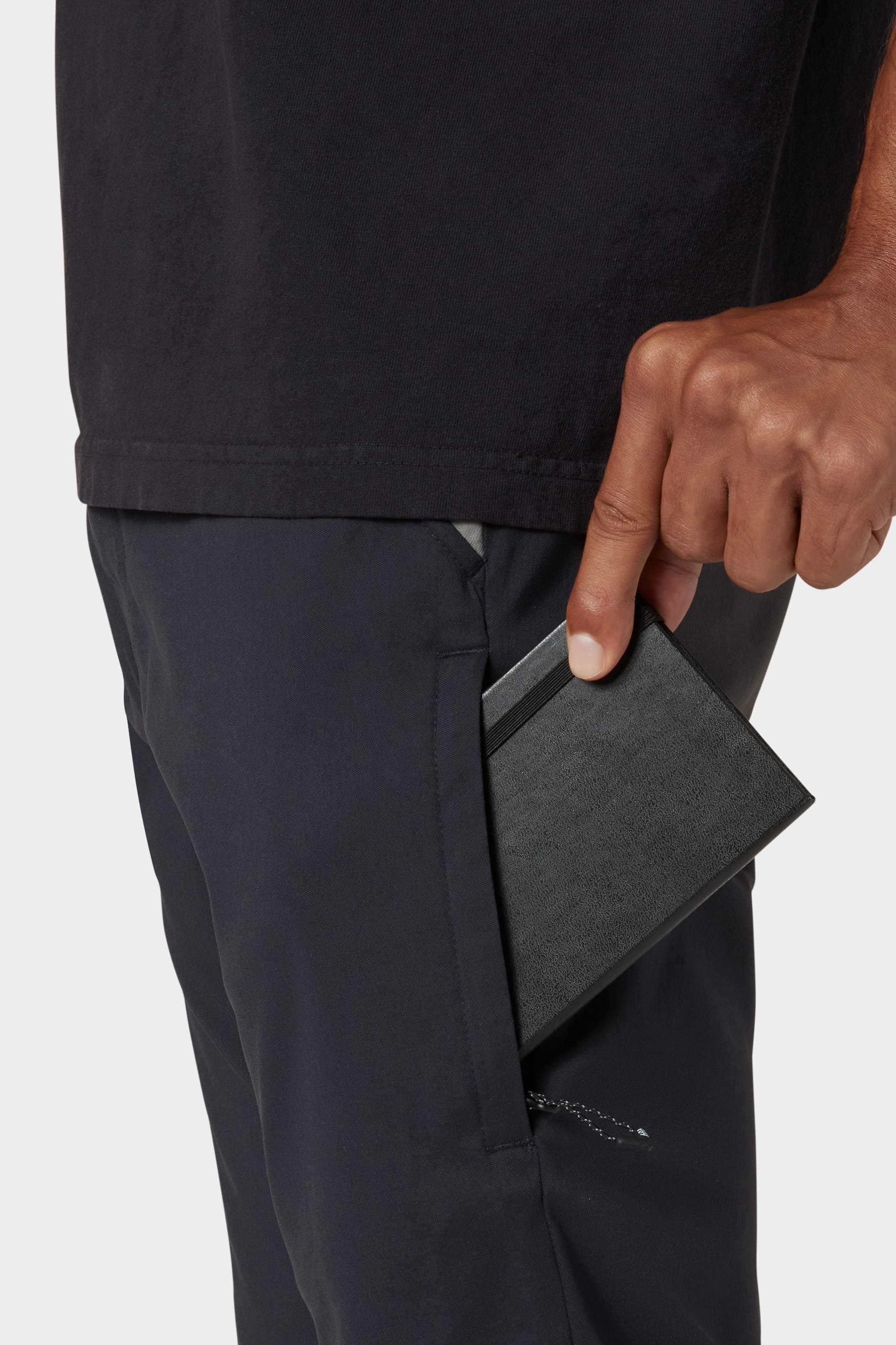 A hand places a black wallet into the front pocket of dark 686 Men's Everywhere® Reclaimed Pant - Slim Fit, cropped to highlight the pocket, part of the shirt, and the subtle, sustainable style of 686's revived fashion.