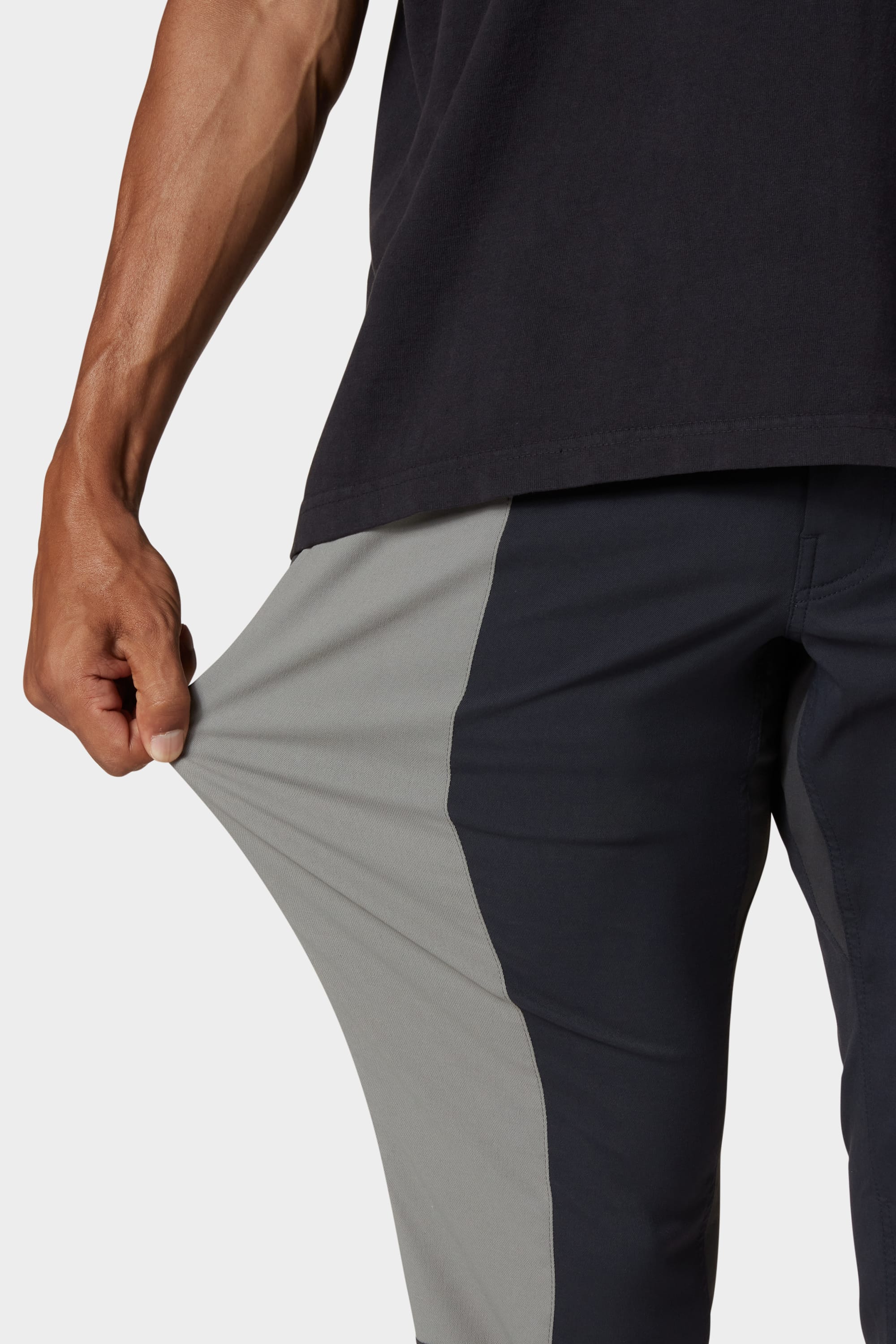 A person wearing 686 Men's Everywhere® Reclaimed Pant - Slim Fit in black and gray stretches the thigh to show the flexible, sustainable fabric; only their arm, hand, and torso are visible, emphasizing comfort and eco-consciousness.