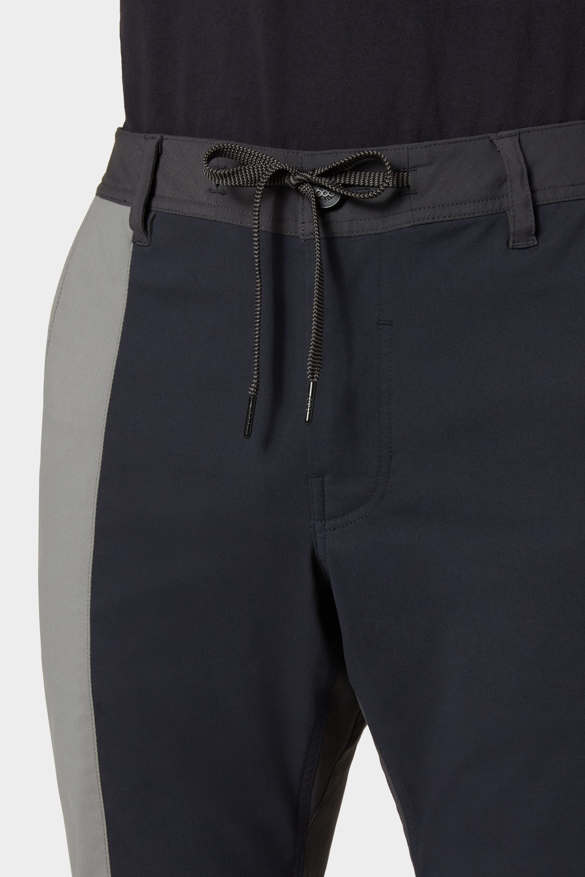 Close-up of a person wearing 686 Men's Everywhere® Reclaimed Pant - Slim Fit, featuring a drawstring waist and light gray side panels, made from deadstock fabrics by 686, paired with a black shirt for a sustainable look.