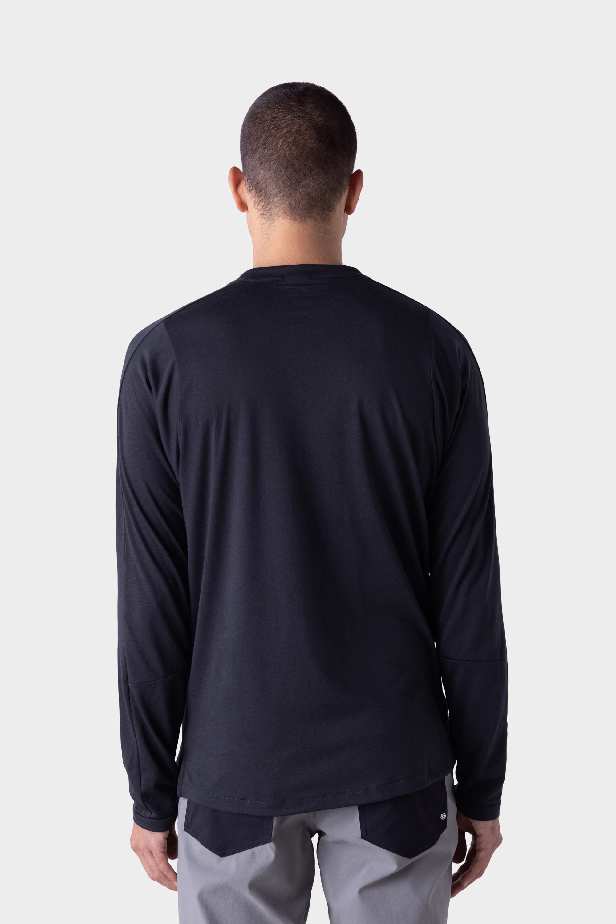 A person with short hair is shown from behind, wearing a black 686 Mens Rival Long Sleeve Bike Jersey and light gray pants against a plain, light-colored background.