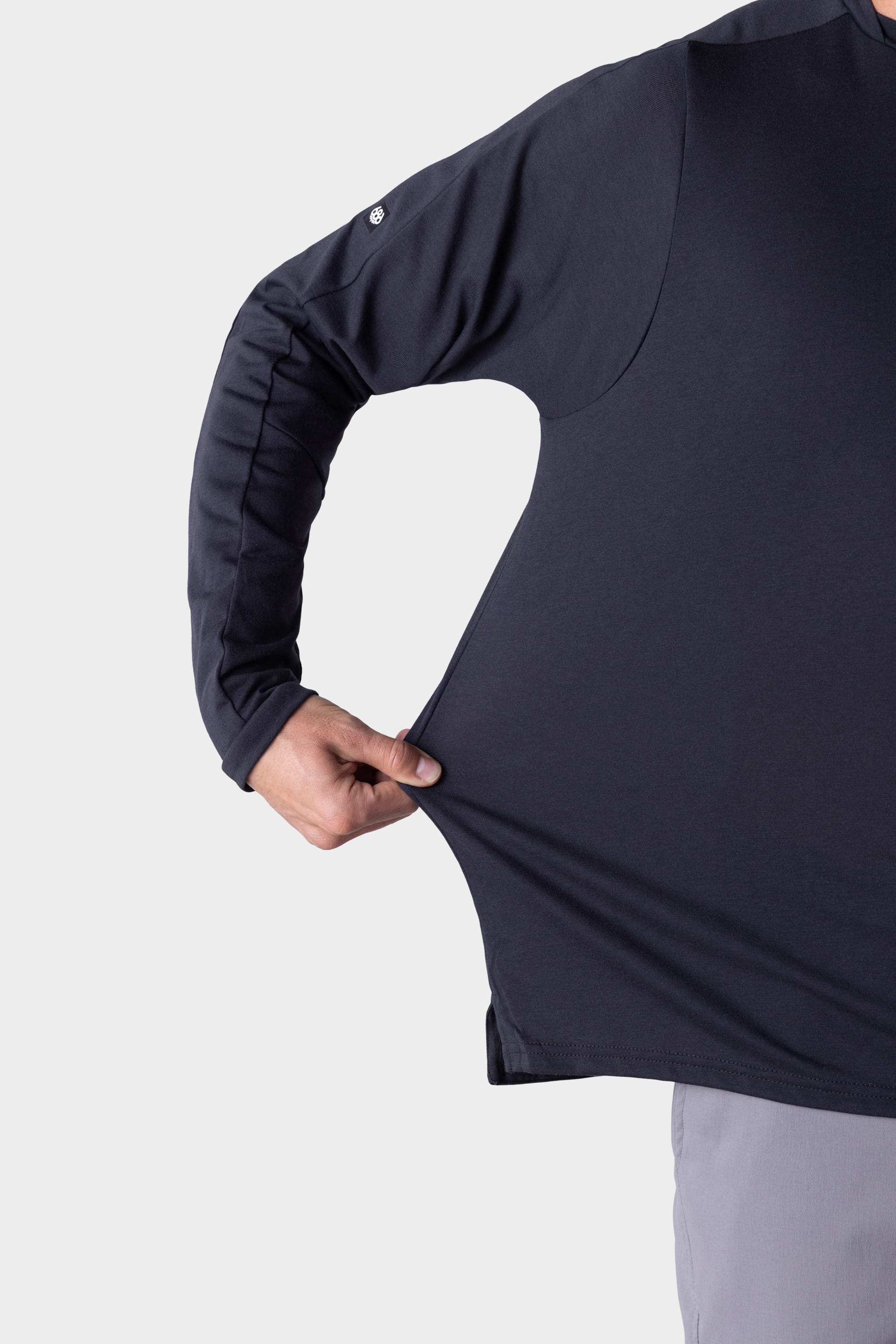 A person wearing the 686 Mens Rival Long Sleeve Bike Jersey stretches the shirt’s side with one hand to show its flexibility. The image is cropped to highlight only the torso and arm.