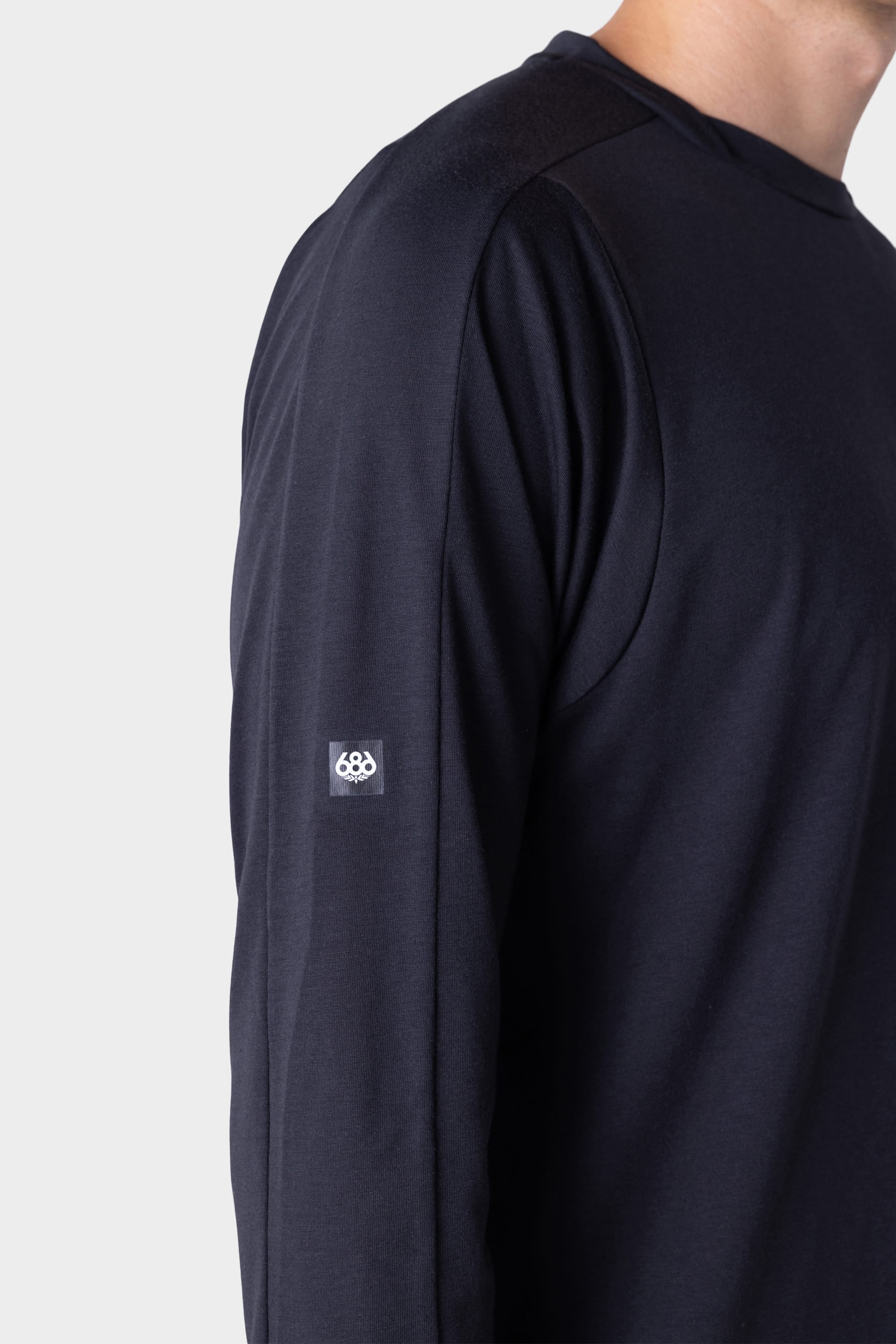 A person wearing the 686 Mens Rival Long Sleeve Bike Jersey in dark navy, featuring a small white 686 logo on the upper arm, stands against a plain light background.