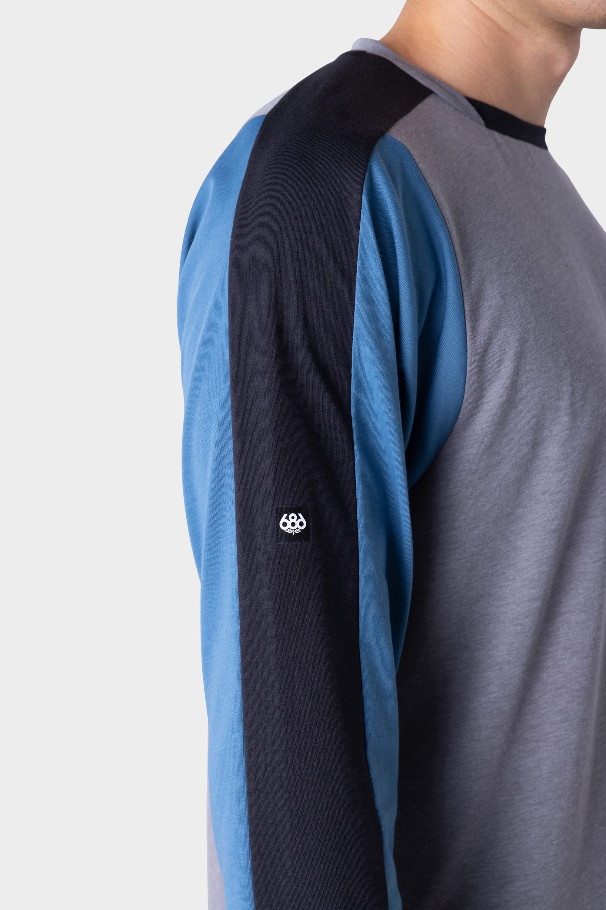 A person wearing the 686 Mens Rival Long Sleeve Bike Jersey, a color-blocked shirt in gray, blue, and black with a small white geometric logo on the sleeve. Only the upper torso and part of their face are visible. Brand: 686.
