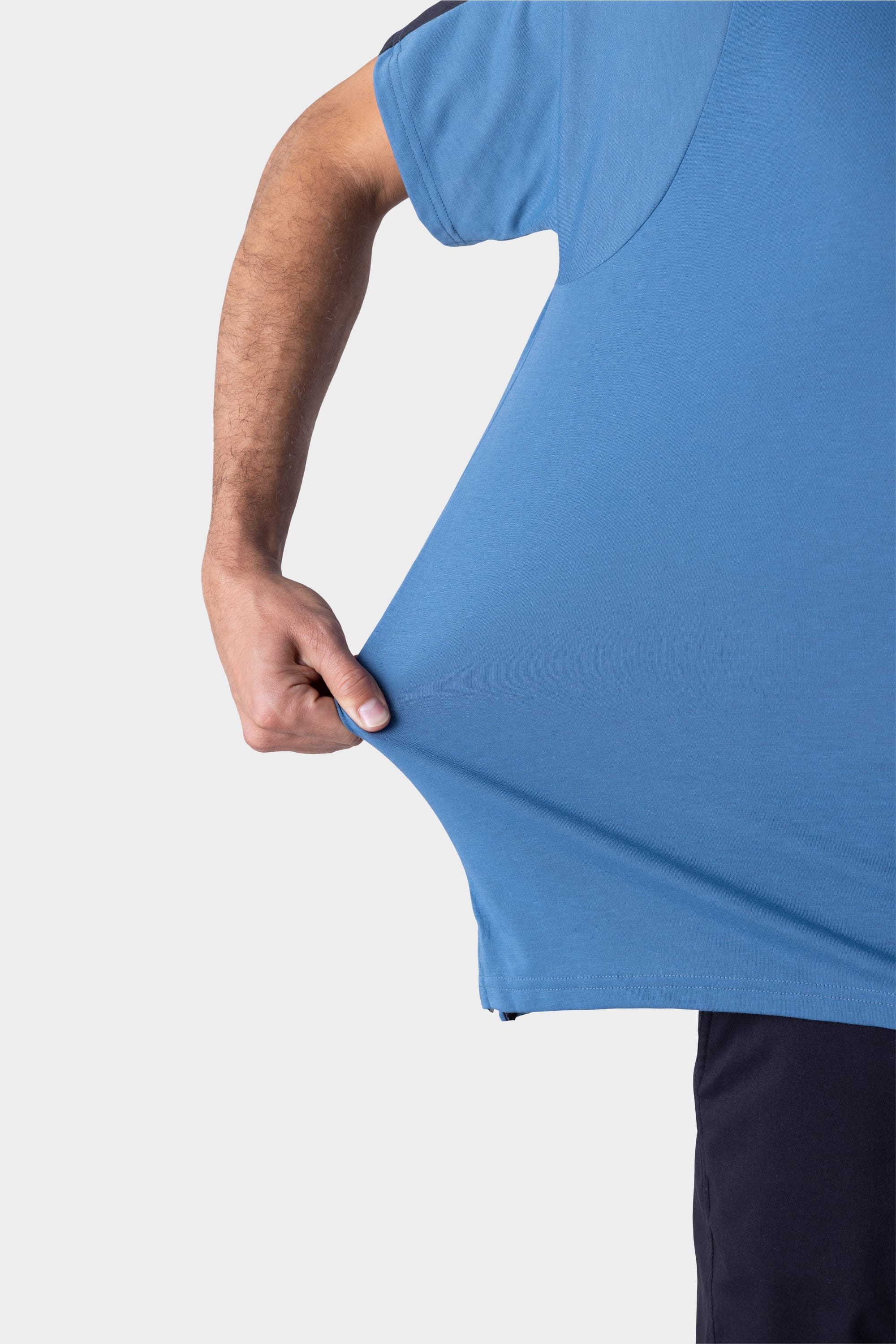 A person wearing the 686 Mens Rival Short Sleeve Bike Jersey stretches the side of their blue jersey with their left hand against a plain white background.