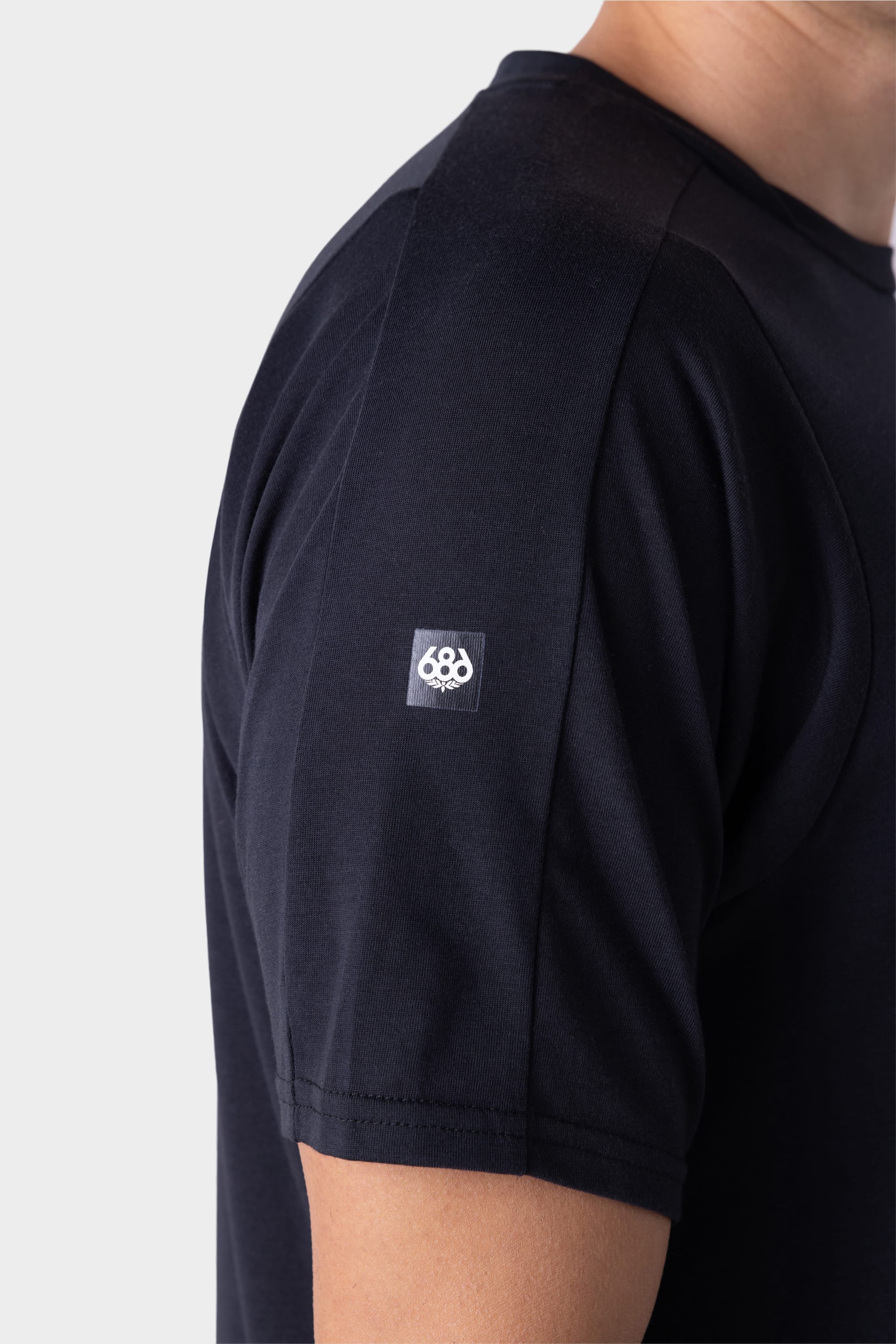 A close-up of a person wearing the 686 Mens Rival Short Sleeve Bike Jersey, featuring a plain black design with a small white 686 logo on the sleeve, highlighting the upper arm and shoulder area.