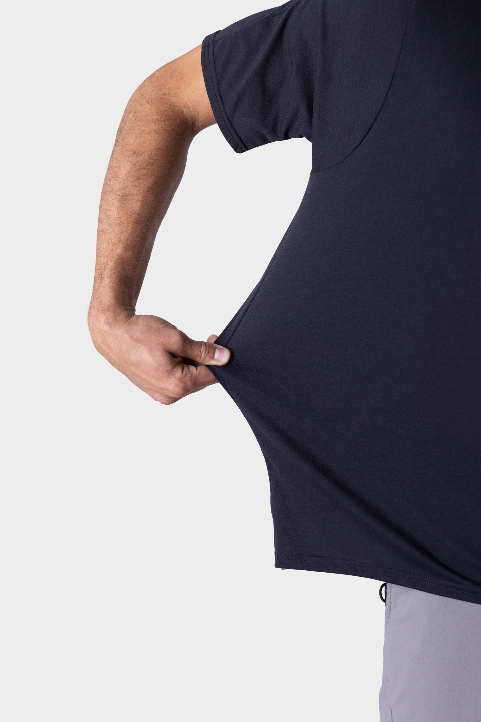 A person wearing the 686 Mens Rival Short Sleeve Bike Jersey by 686 stretches the side of the jersey outward with their left hand against a plain, light background.