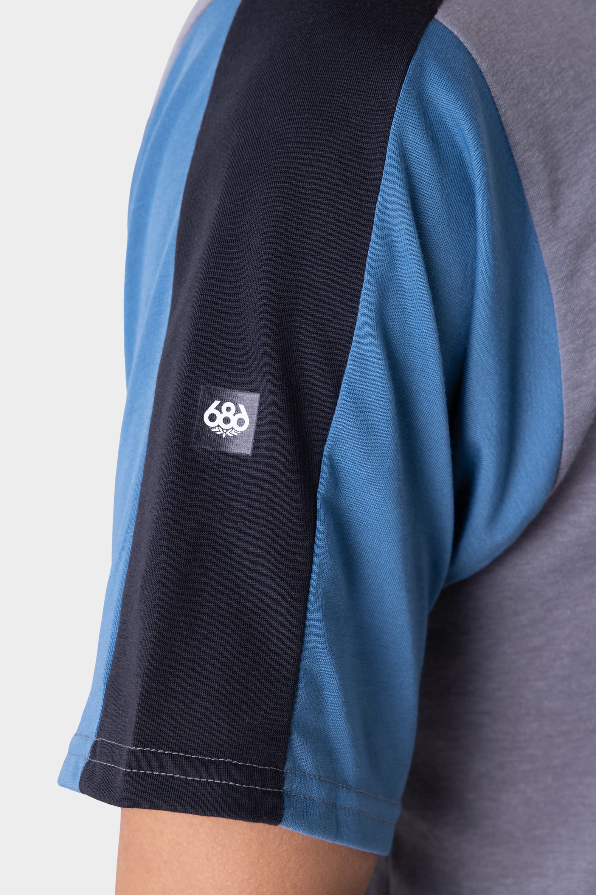 Close-up of a persons upper arm in the 686 Mens Rival Short Sleeve Bike Jersey, featuring blue, black, and gray color blocks and a small white 686 logo patch on the sleeve.