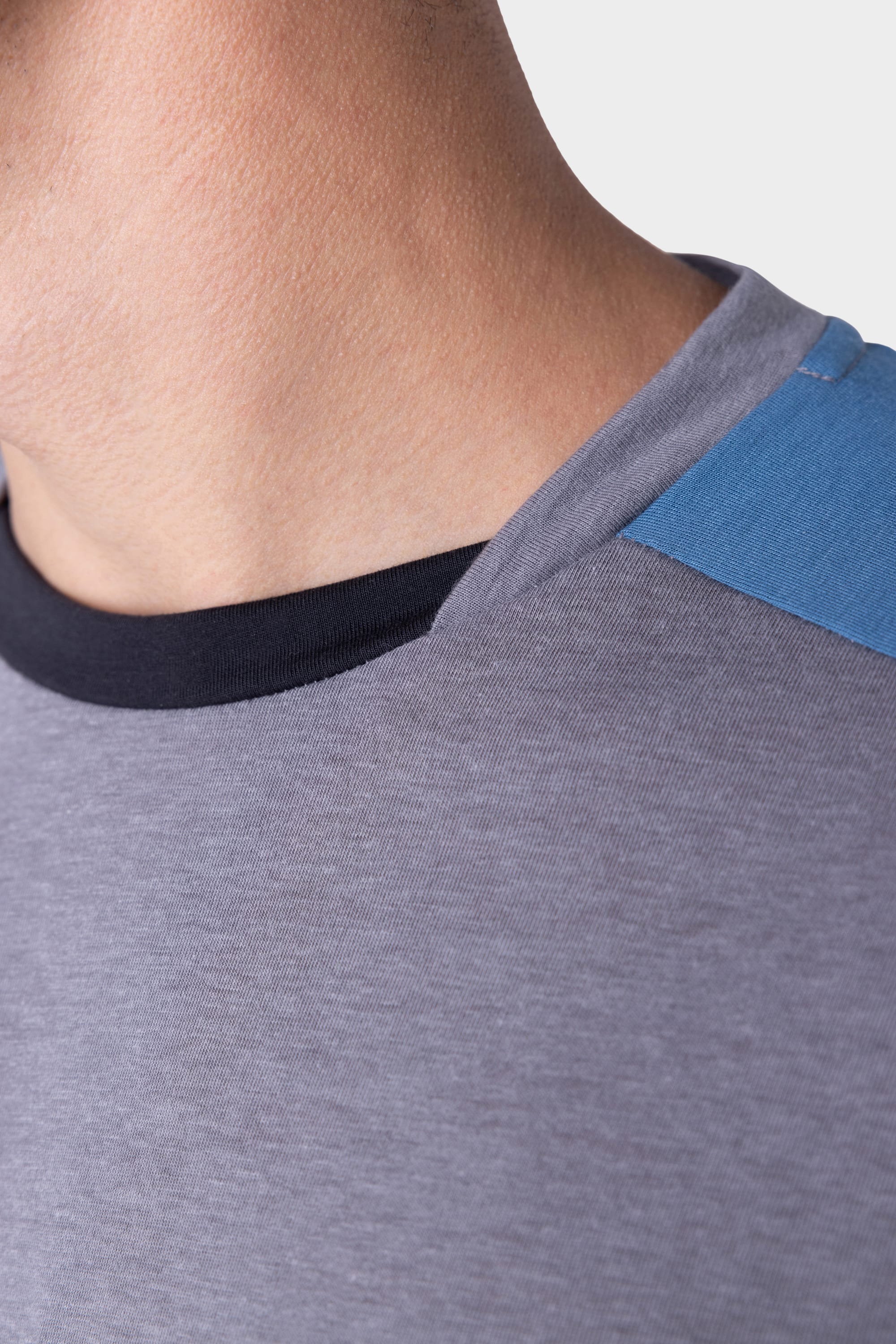 Close-up of a person wearing the 686 Mens Rival Short Sleeve Bike Jersey—a grey tee by 686 featuring a black collar and blue shoulder patch. The background is plain and light-colored.