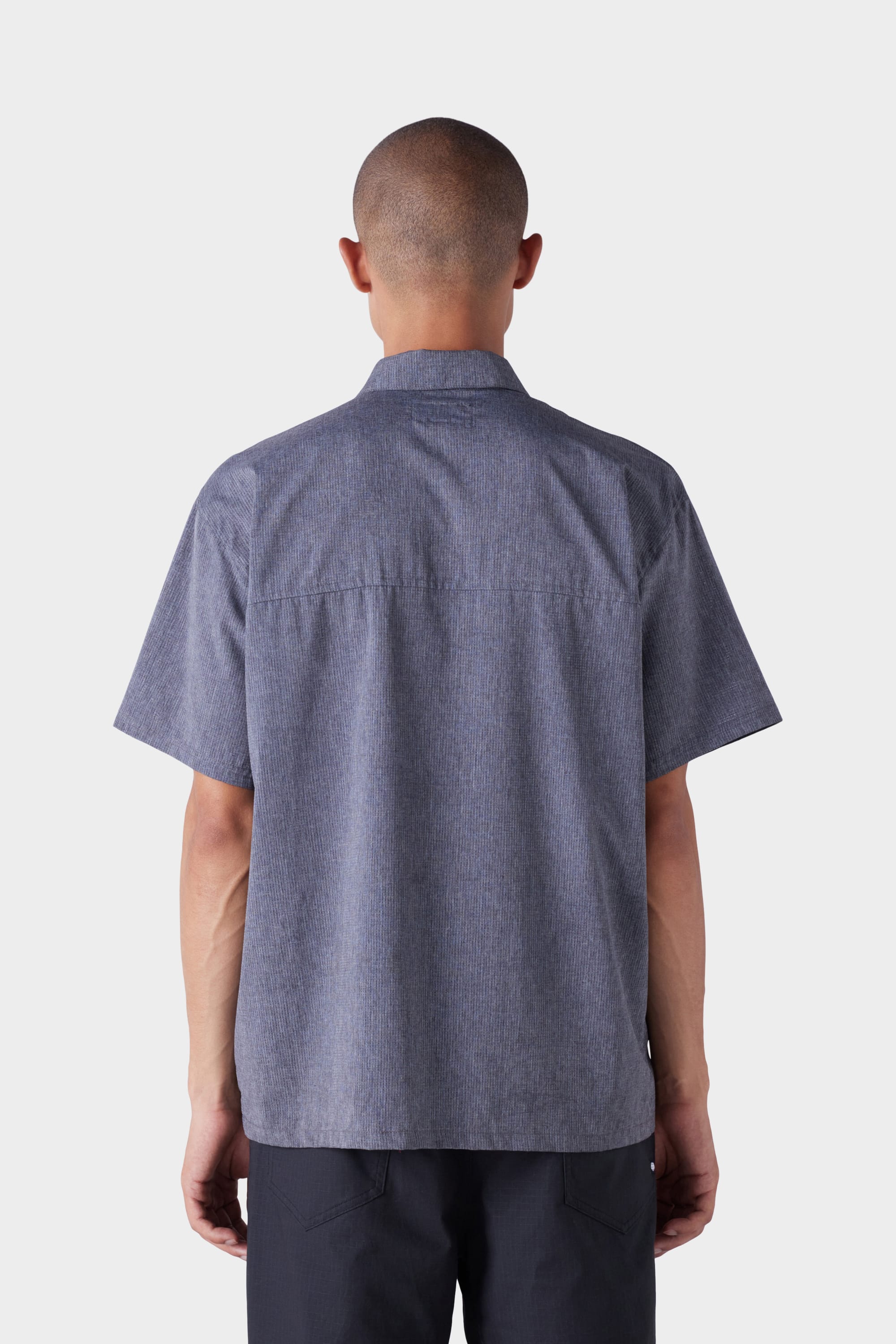A person with short hair is seen from behind, wearing the 686 Mens Seeker Perforated Button Up by 686 in dark gray with dark pants, set against a plain light background.