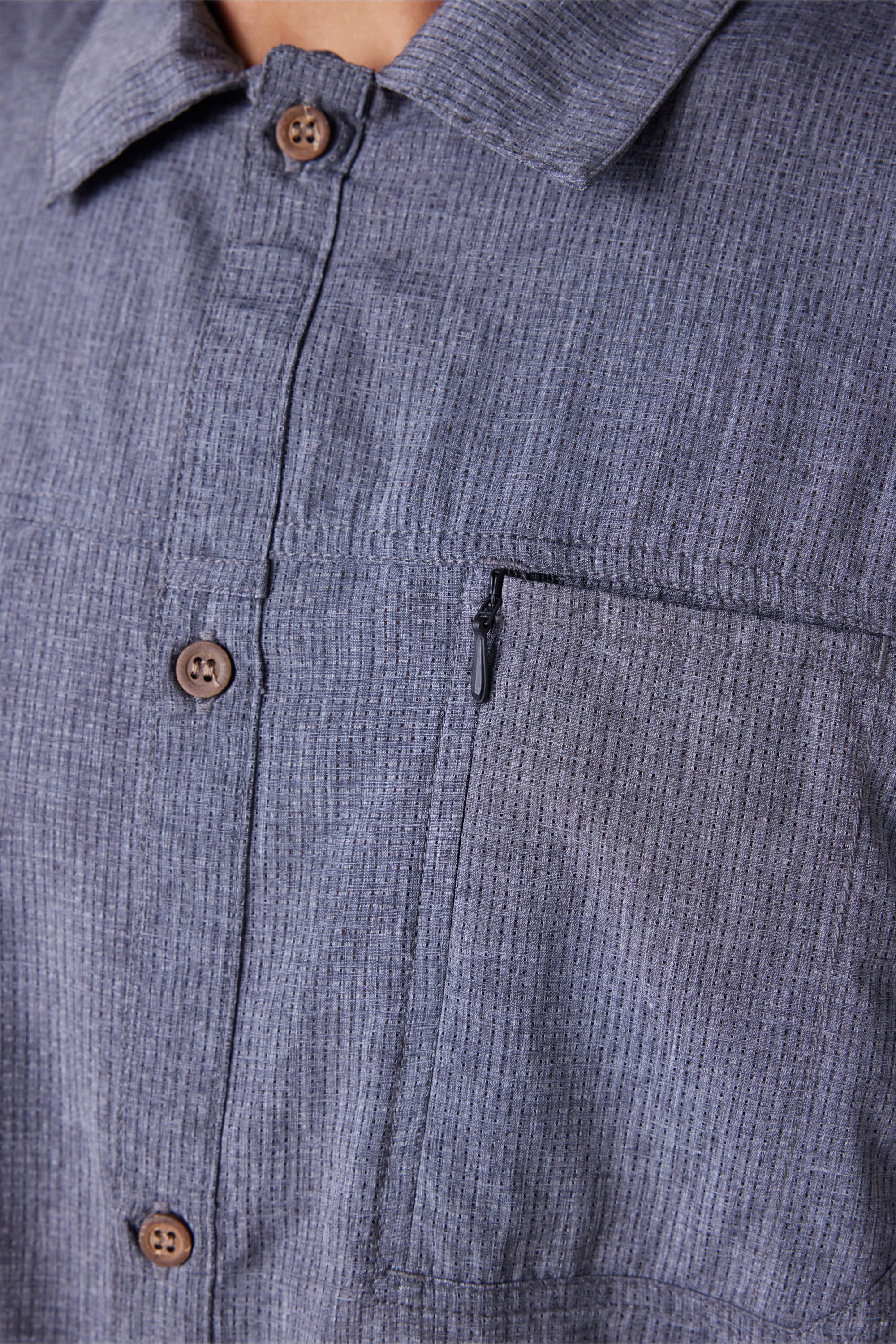 Close-up of the 686 Mens Seeker Perforated Button Up shirt in blue-gray with vertical stripes, brown buttons, and a zippered left chest pocket. Only the upper torso is shown.
