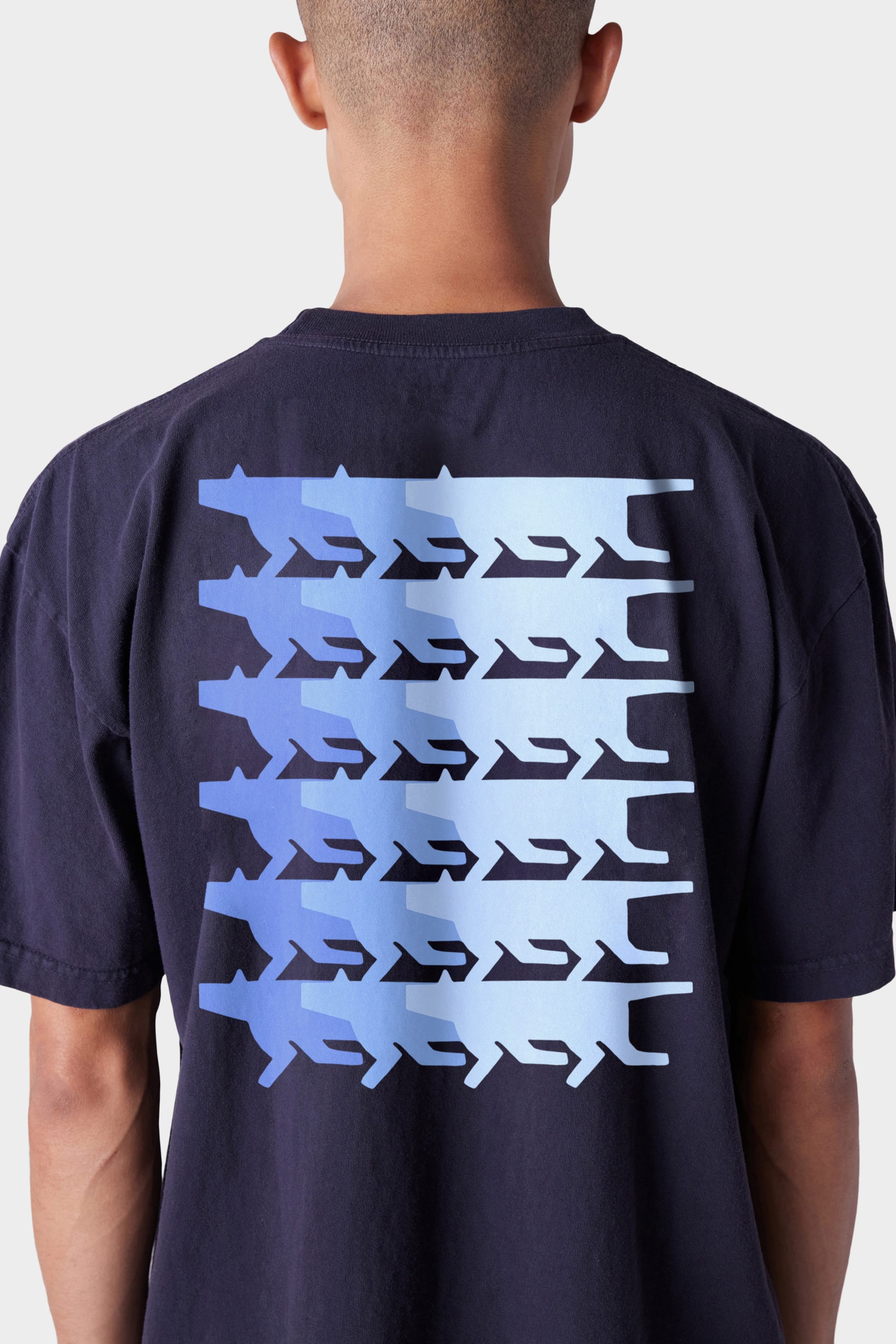 A person wearing the 686 Mens Wanderers Short Sleeve Tee by 686, which features a back graphic of six horizontal rows of stylized blue sharks on a light background.