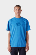 A person with short hair wears the 686 Mens Wreath Short Sleeve Tee—a loose-fitting blue T-shirt by 686 featuring a chest design—while standing facing forward against a plain white background.