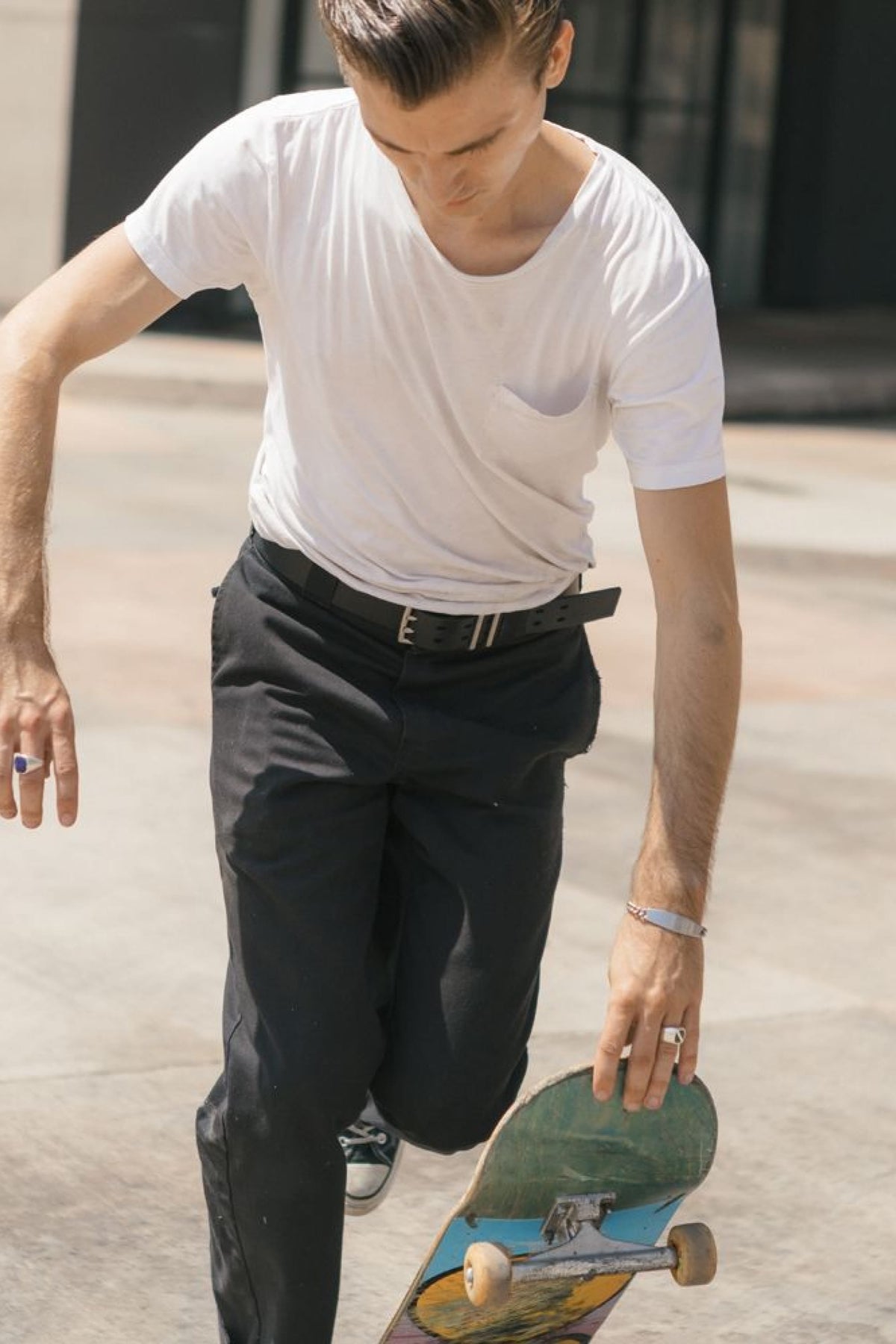 Someone is outdoors on a sunny day, bending forward with a skateboard while wearing the 686 Westwell Voyager Belt from 686.