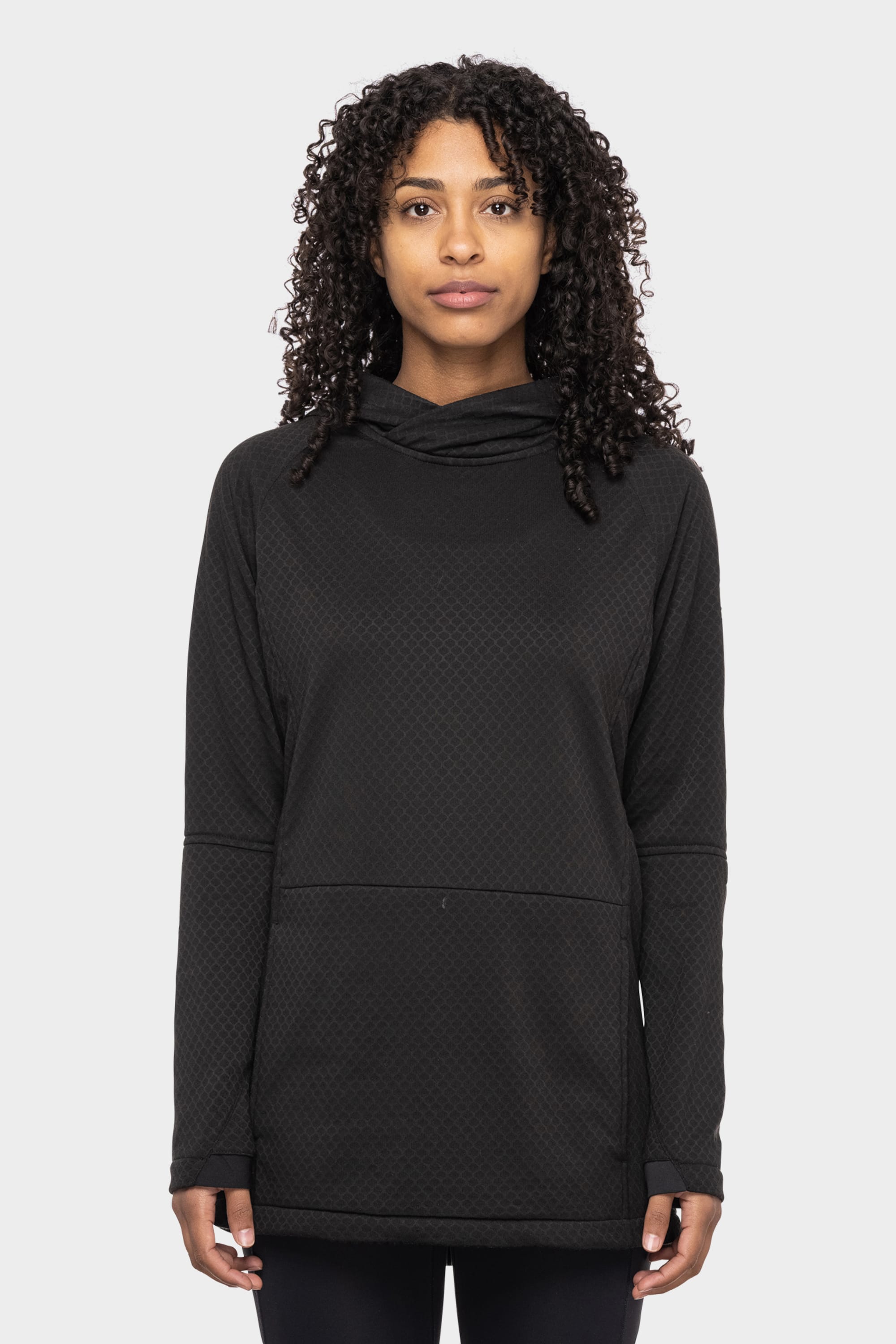 A woman with curly hair wears the 686 Women's Mission Gridª Fleece Hoody, a black textured long-sleeve hoodie by 686, while standing facing forward against a plain white background.