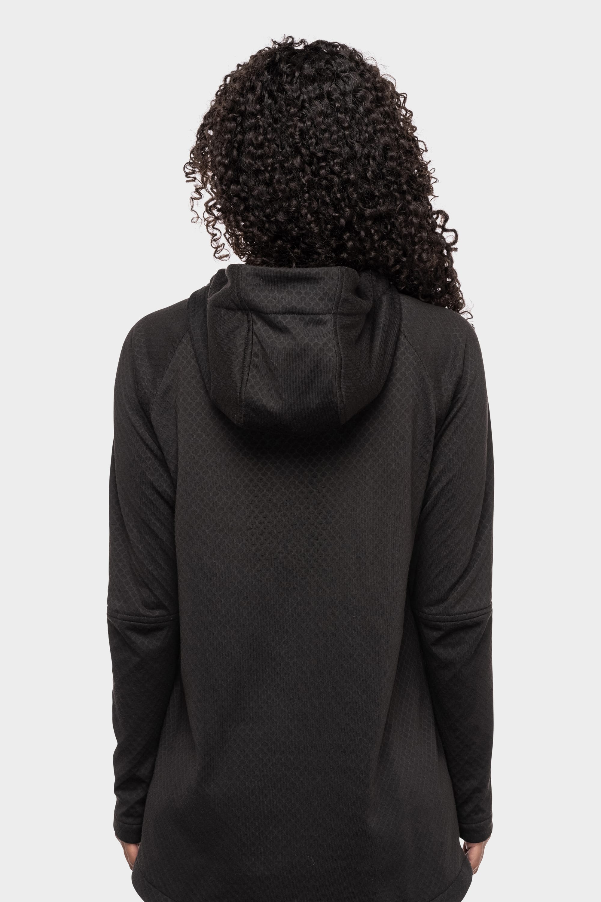 A woman with curly hair, seen from behind, wears the 686 Women's Mission Gridª Fleece Hoody by 686 in black against a plain white background.