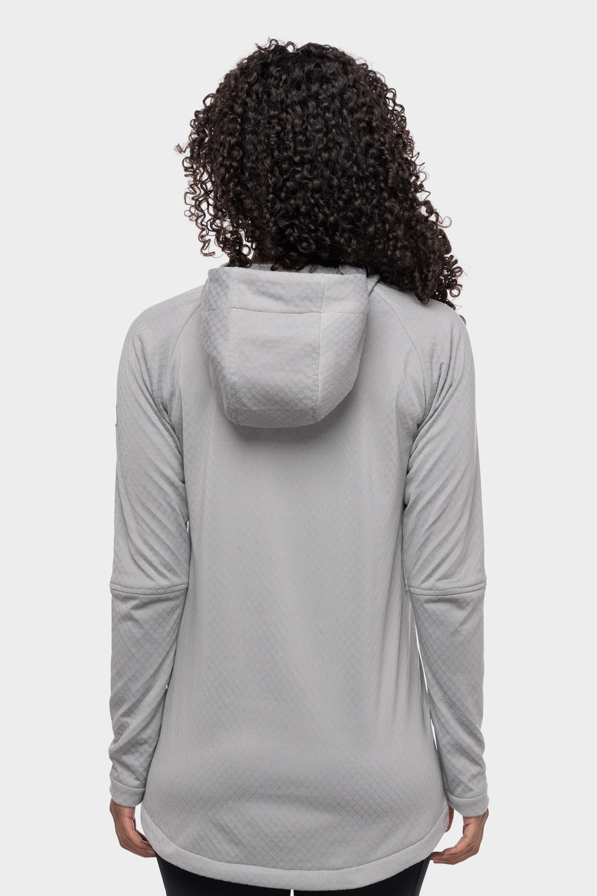 A person with curly hair is seen from the back wearing the 686 Women's Mission Gridª Fleece Hoody in light gray by 686, featuring long sleeves and a hood, set against a plain white background.