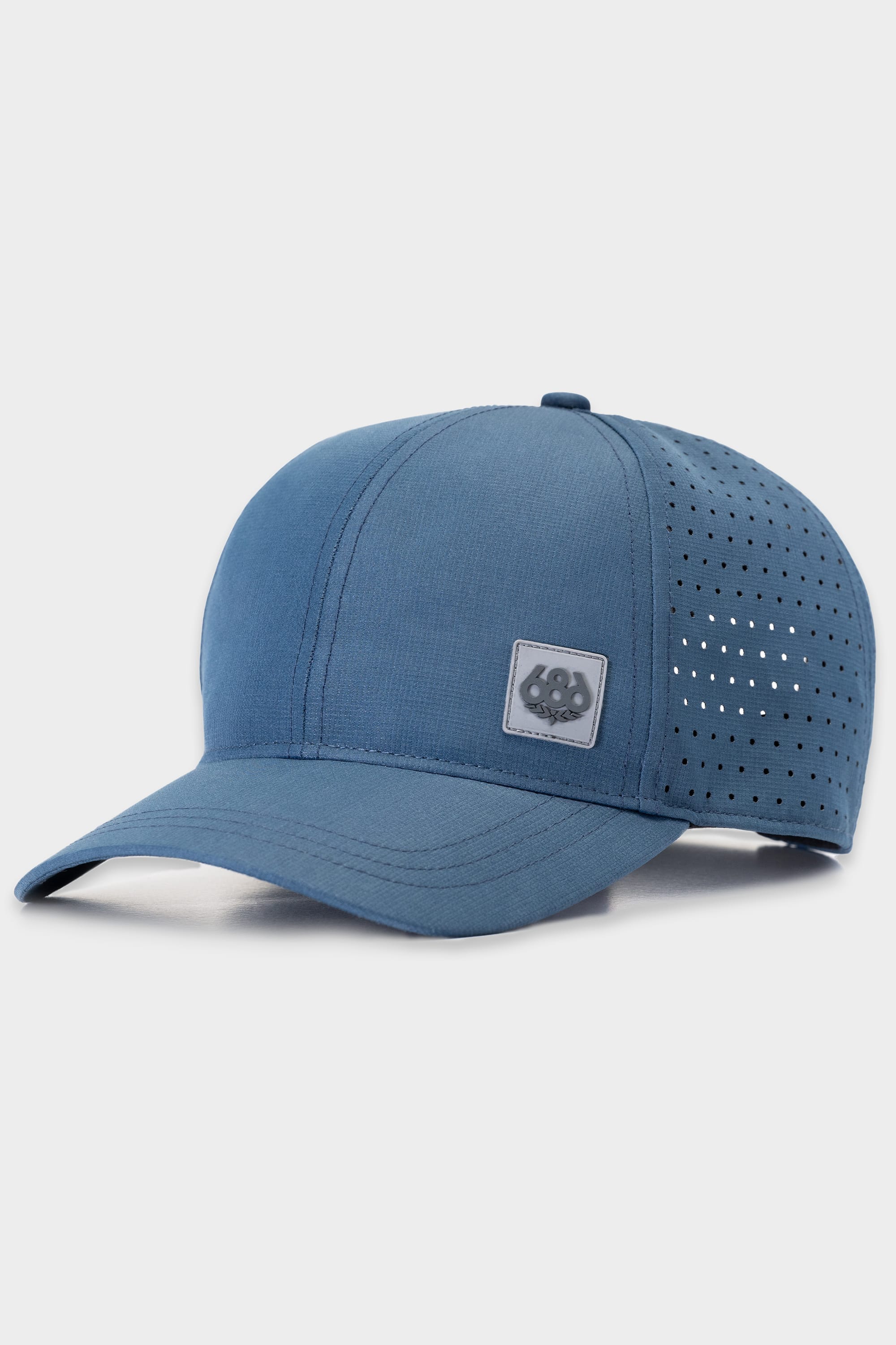 The 686 Perforated Hat is a blue baseball cap from 686 with a curved brim, side ventilation holes, and a small front square patch bearing a paw print logo.