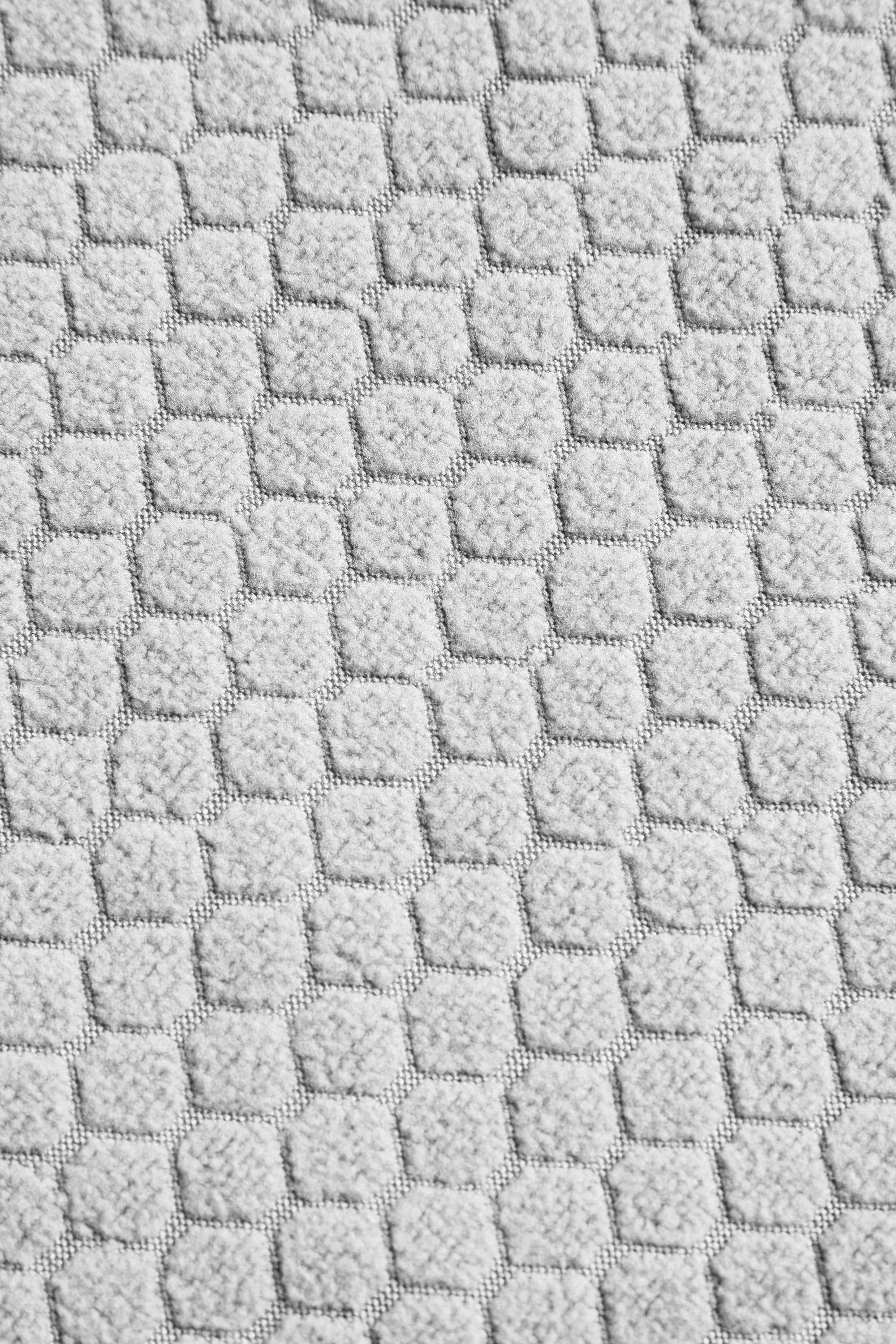 Close-up of the 686 Women's Mission Gridª Fleece Hoody by 686, featuring light gray textured fabric with a repeating pattern of small, raised hexagons in neat rows and columns.