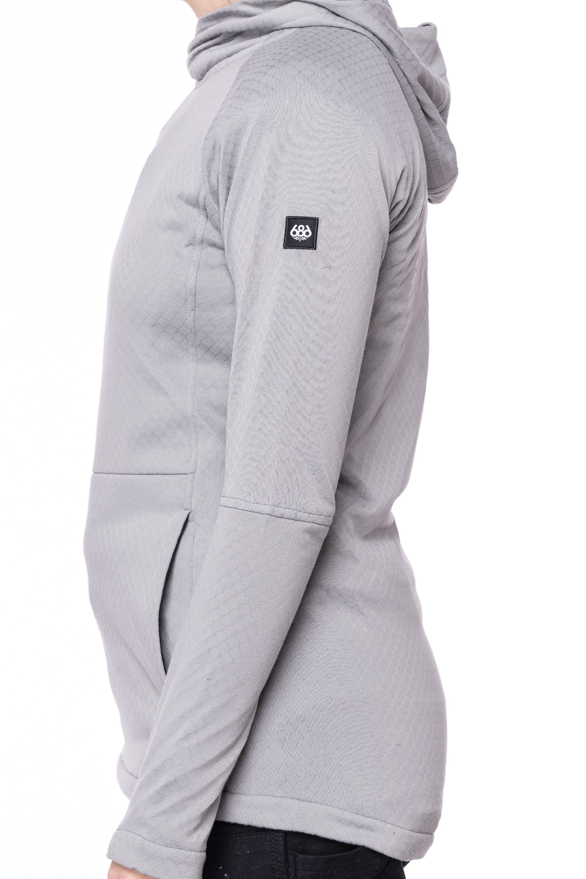 A woman wearing the 686 Women's Mission Gridª Fleece Hoody in light gray, featuring long sleeves, a hood, and a small black logo patch on the upper sleeve, is shown from the side against a white background.