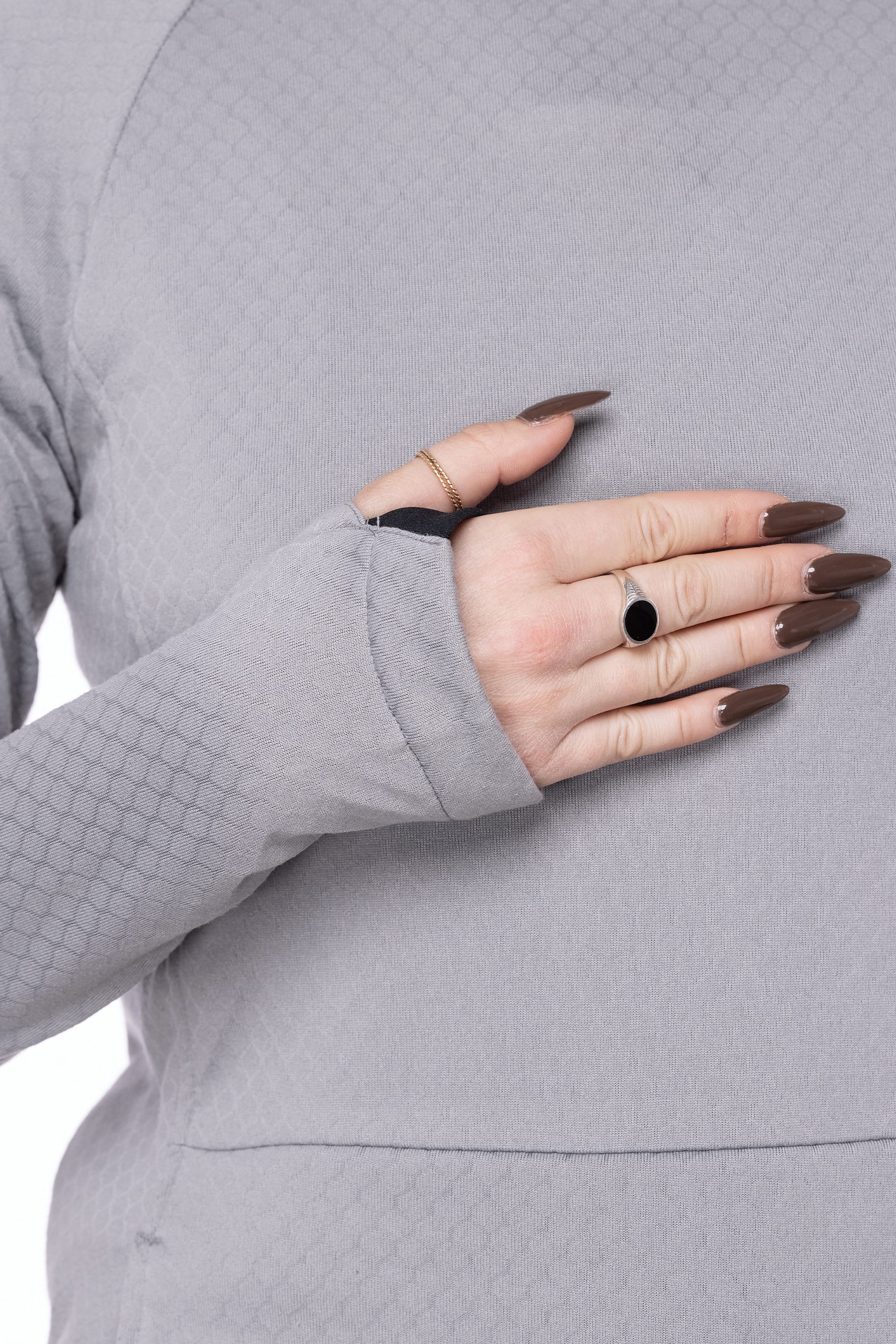 A person wearing the 686 Women's Mission Gridª Fleece Hoody in light grey, featuring a thumbhole, displays manicured nails and rings while resting their hand on their chest.