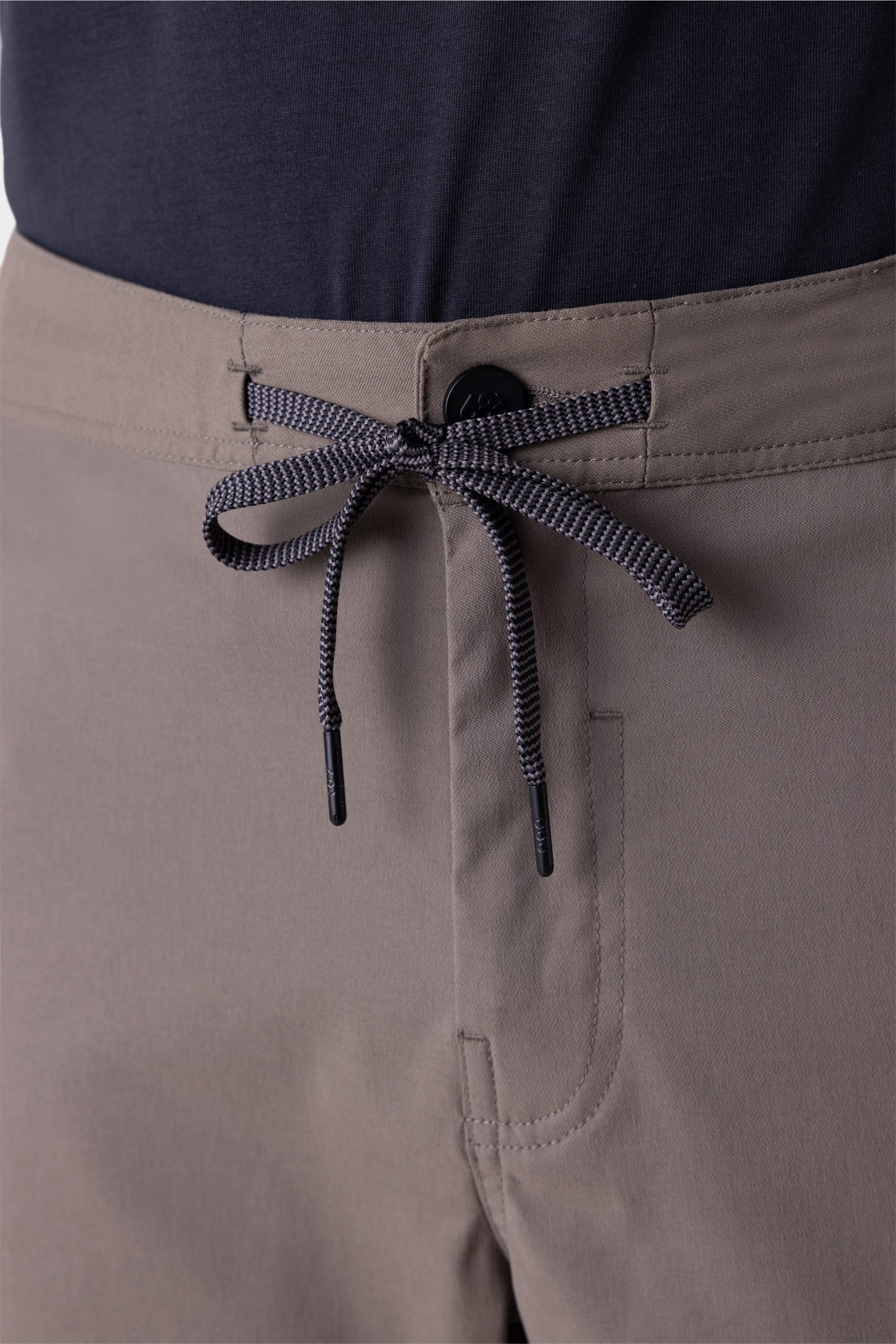 Close-up of a person wearing the 686 Mens Platform Bike Pant - Relaxed Fit in taupe with a black and white drawstring waist, paired with a tucked-in dark shirt.