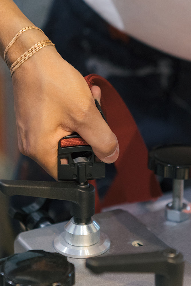 A close-up of a person‚Äôs hand tightening the red 686 Westwell Clicker Stretch Belt from 686, possibly securing equipment, while wearing gold chain bracelets.